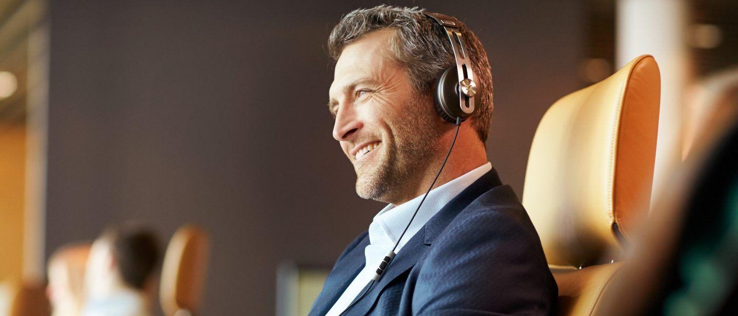 A man enjoys music on his headphones in his Lufthansa First Class seat, which can be enjoyed with a cheap flight with Flight Centre.