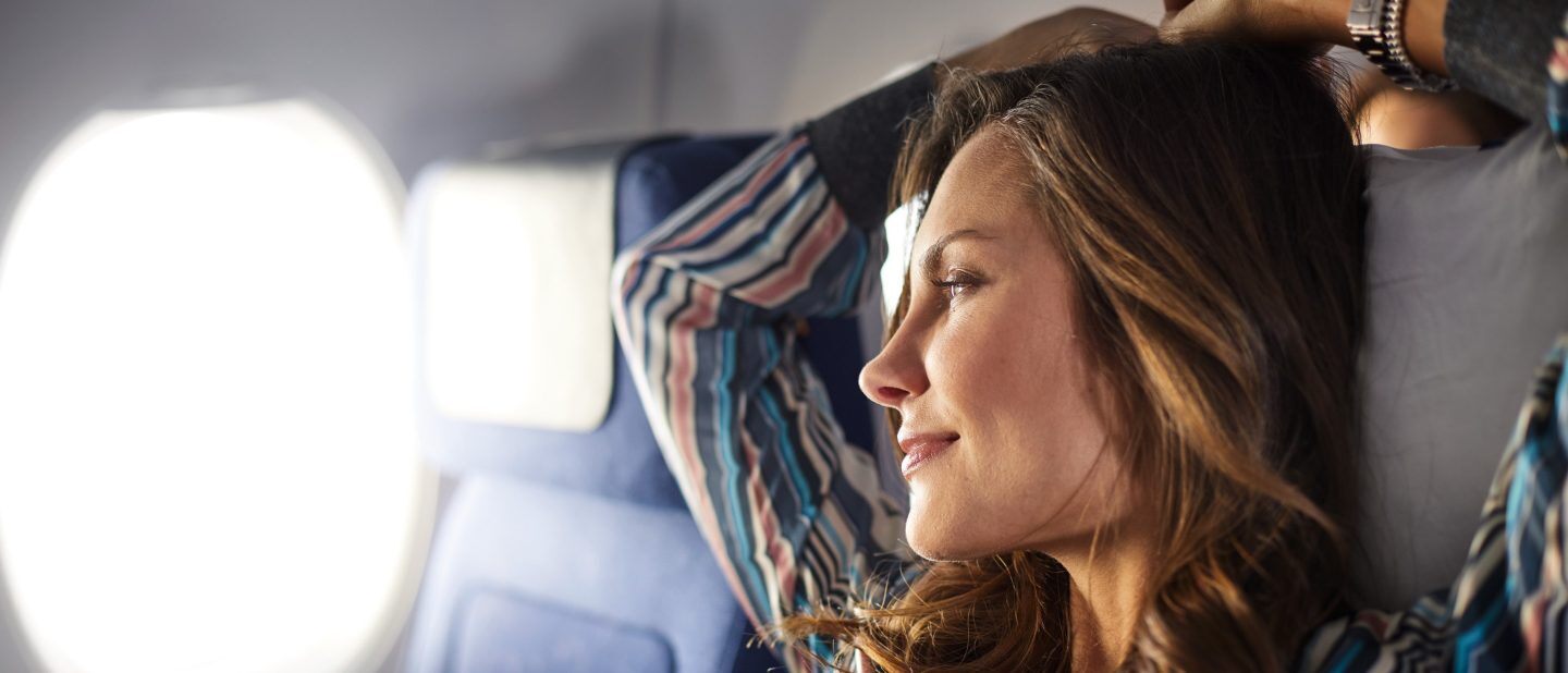 A woman enjoys the view out of the window in her Lufthansa Economy Class seat, which can be enjoyed with a cheap flight with Flight Centre.
