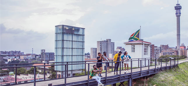 A crowd of people lean against the rails of a bridge in Johannesburg, where you can book hotels and other accommodation with Flight Centre.