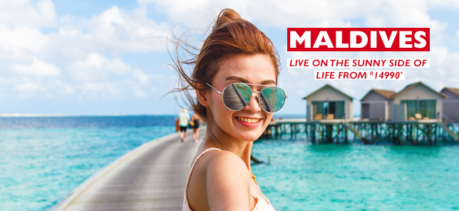 A woman smiles in front of her overwater bungalow in the Maldives, which can be enjoyed with a holiday package from Flight Centre.