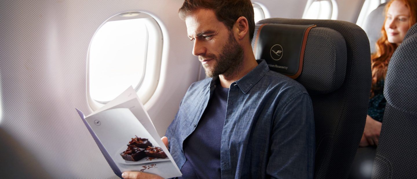 A man reads a menu in his Lufthansa Premium Economy Class seat, which can be enjoyed with a cheap flight with Flight Centre.