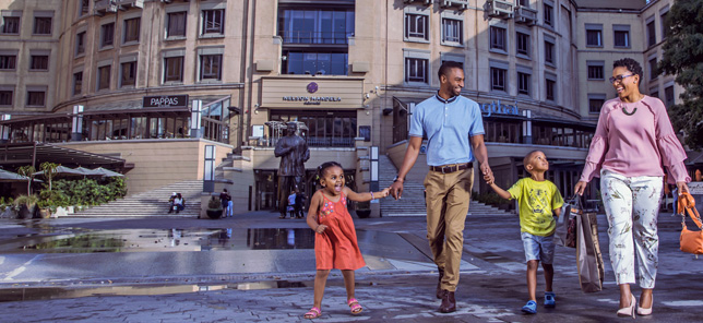 A family smile while walking through Nelson Mandela Square in Sandton, which can be visited when you book your hotel or other accommodation with Flight Centre.